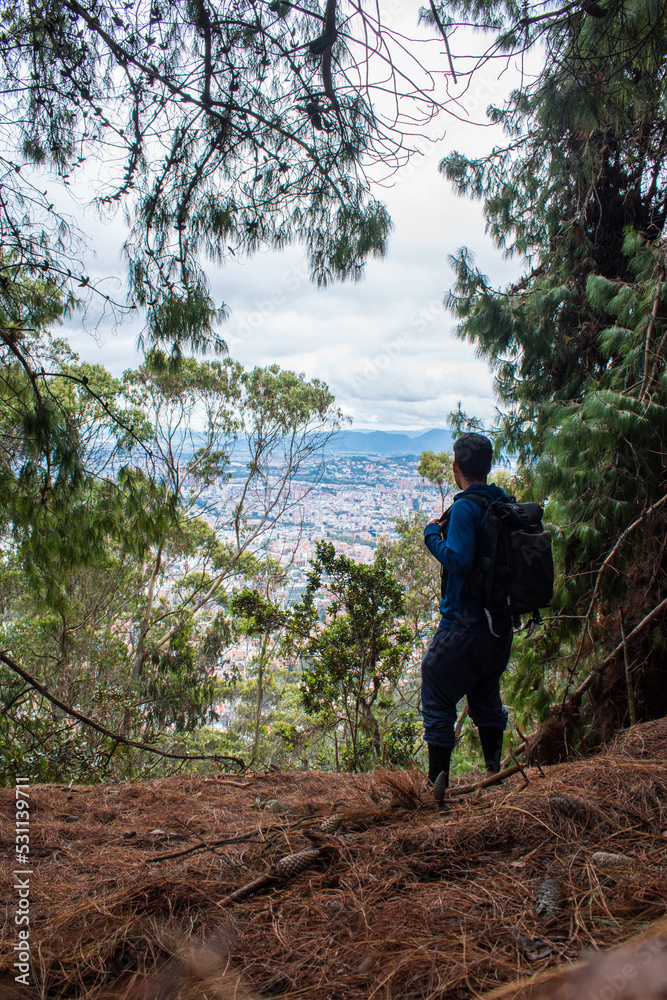 Young man walkingon forest mountain path next to a big city Young man walkingon forest mountain path next to a big city