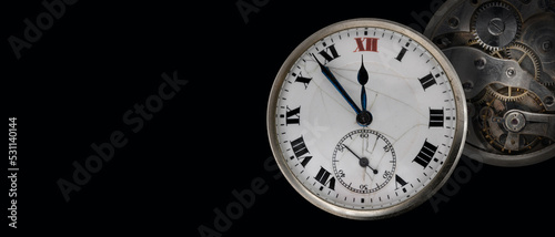 An old antique clock with roman numerals on the dial and clockwork isolated on black background