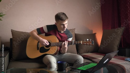 young man is learn.ing to play the acoustic guitar. online learning.