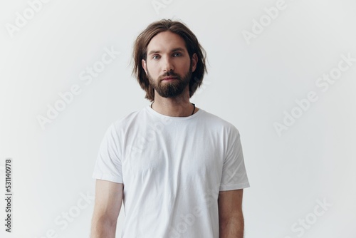 Fotografia Portrait of a man with a black thick beard and long hair in a white T-shirt on a