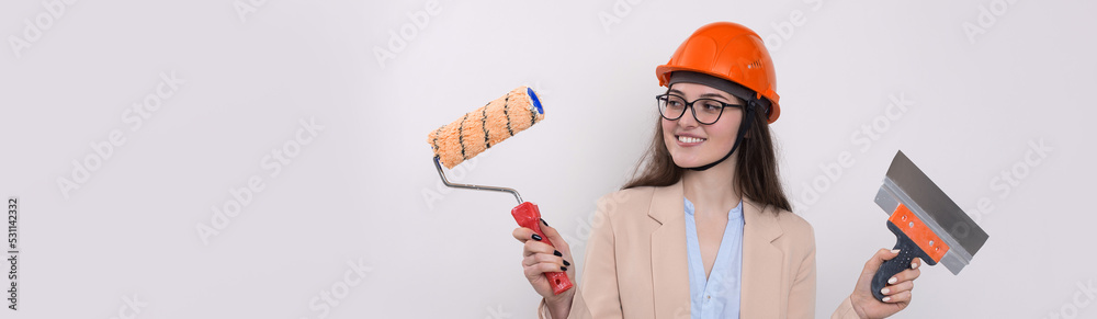 Girl engineer in an orange construction helmet with plastering painting tools in her hands on a white background. Girl engineer in an orange construction helmet with plastering painting tools in her hands on a white background.