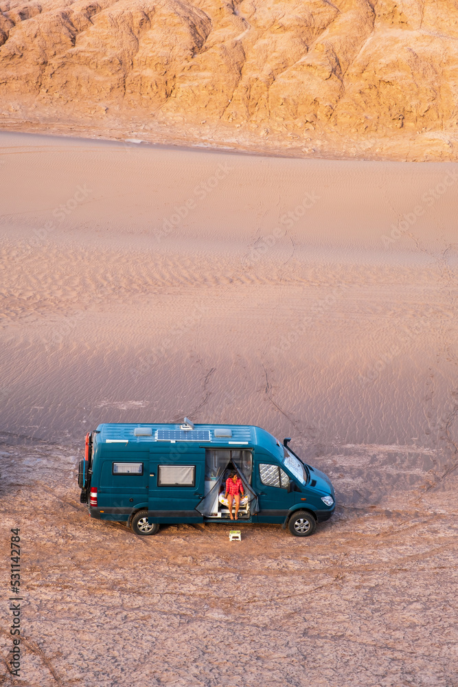 Woman sitting in her campervan in the desert at sunset