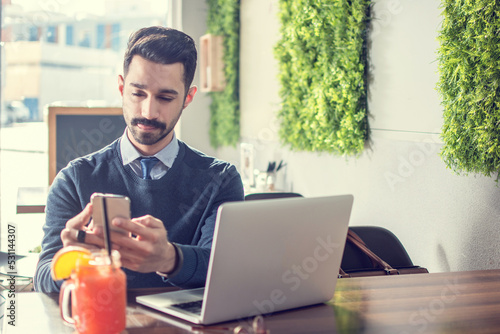 Canvas Print Focused young handsome business man replying to text message on mobile phone licking lips, showing tongue and frowning as staring smartphone display at cafe