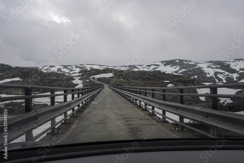 Sauda, Norway - June 10, 2022:  Staudamm on the  Svartavatnet lake. POV from a Tesla Model 3 dual motor long range  with tinted windows and aero wheels in a cloudy spring day. Selective focus photo