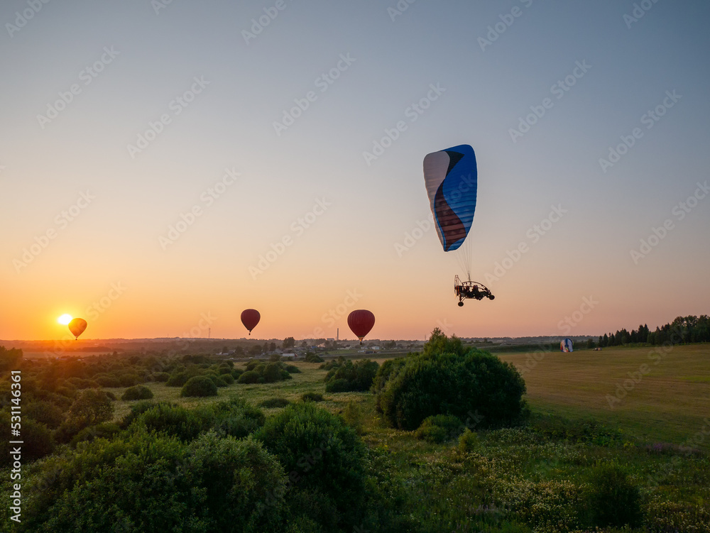 Obraz premium Colorful air balloon is flying in free flight over the field. Bird's-eye view. Multicolored balloon in the sky at sunset