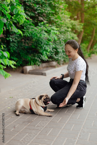 Young girl goes for walk with doggy pug in park. Selective focus.