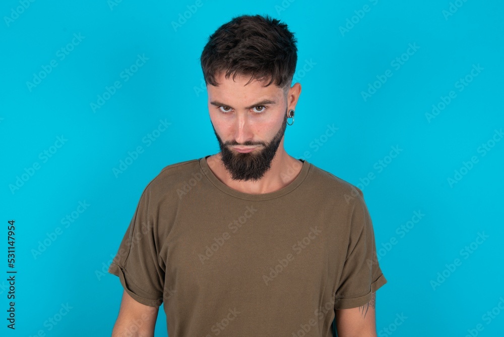 young bearded hispanic man wearing casual clothes over blue background Pointing down with fingers showing advertisement, surprised face and open mouth