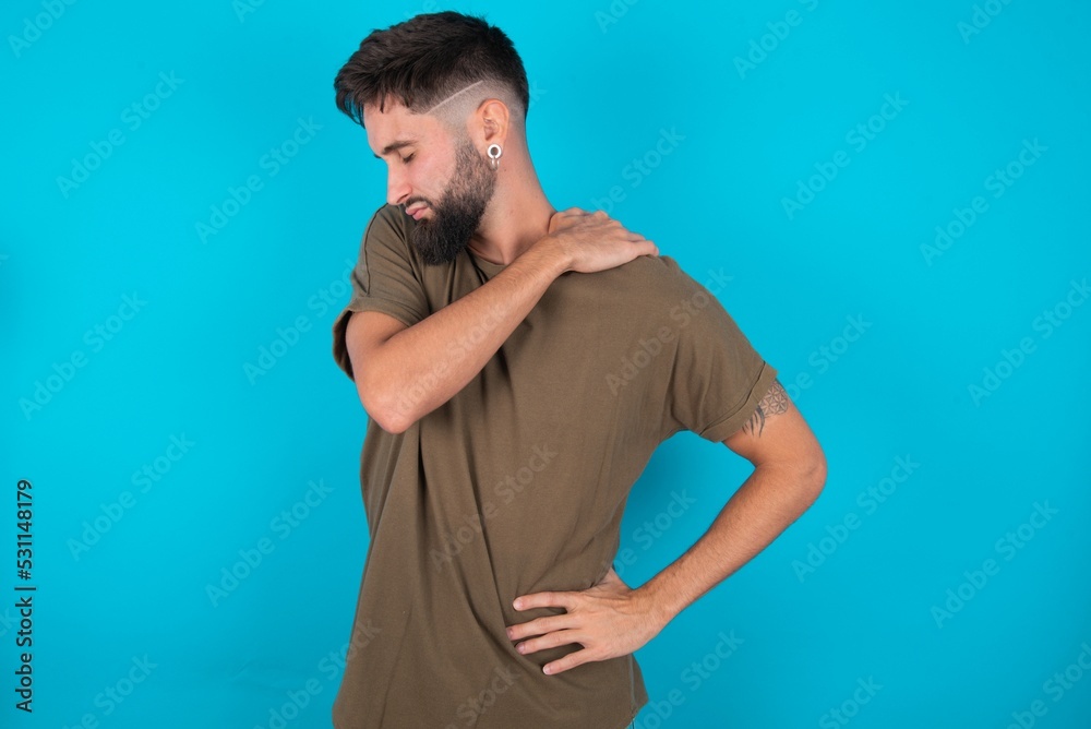 young bearded hispanic man wearing casual clothes over blue background got back pain young bearded hispanic man wearing casual clothes over blue background got back pain