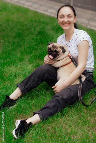 Young girl goes for walk with doggy pug in park. Selective focus.
