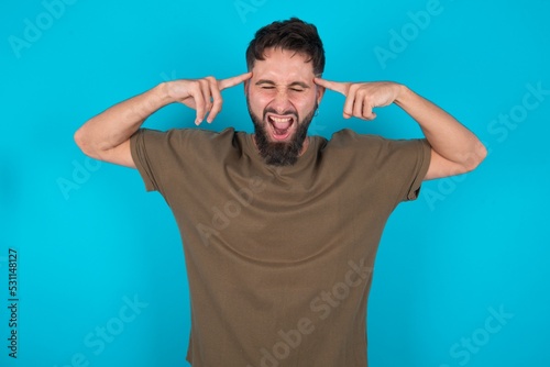 Photo of crazy young bearded hispanic man wearing casual clothes over blue background screaming and pointing with fingers at hair closed eyes