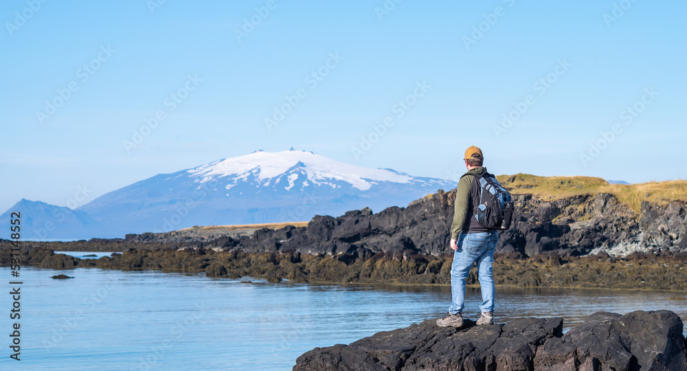person standing on the edge of the water looking at the mountain