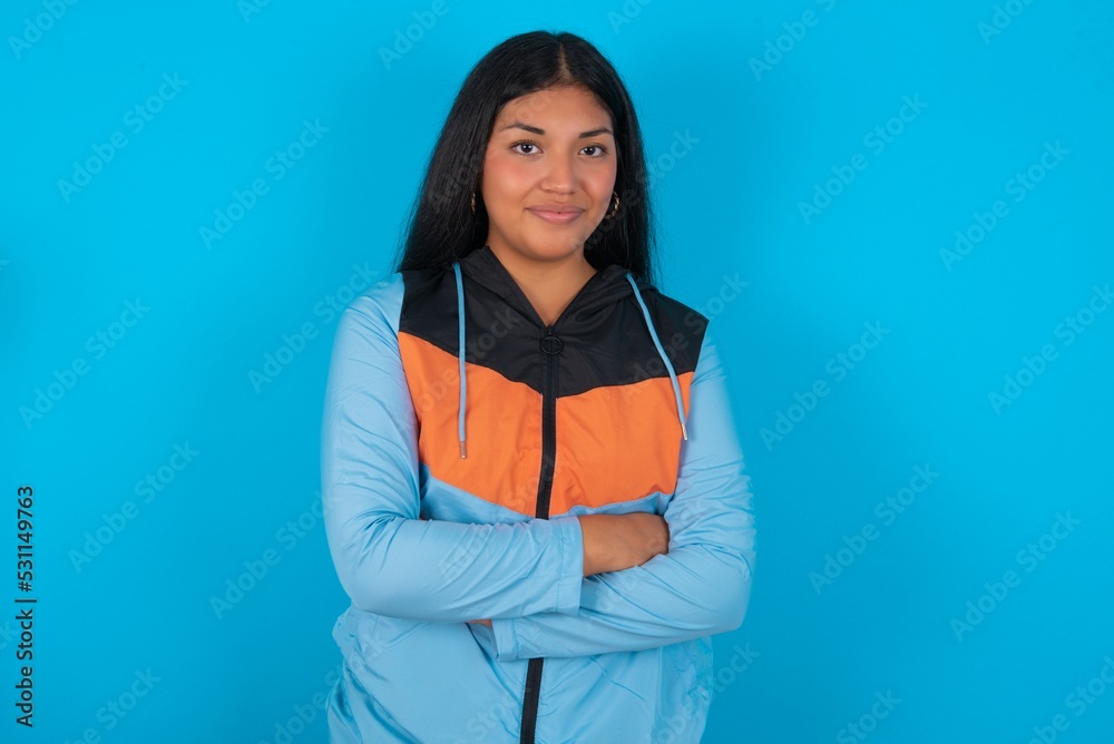 Waist up shot of self confident young beautiful latin woman wearing sportswear has broad smile, crosses arms, happy to meet with colleagues. Waist up shot of self confident young beautiful latin woman wearing sportswear has broad smile, crosses arms, happy to meet with colleagues.
