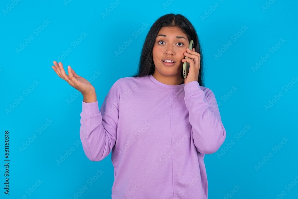 young beautiful latin woman wearing casual clothes standing aga talking on the phone stressed with hand on face, shocked with shame and surprise face, angry and frustrated. Fear and upset for mistake. young beautiful latin woman wearing casual clothes standing aga talking on the phone stressed with hand on face, shocked with shame and surprise face, angry and frustrated. Fear and upset for mistake.