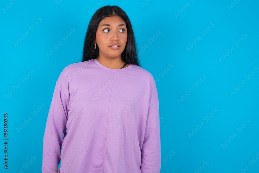Young beautiful hispanic woman wearing casual clothes over blue background stares aside with wondered expression has speechless expression. Embarrassed model looks in surprise Young beautiful hispanic woman wearing casual clothes over blue background stares aside with wondered expression has speechless expression. Embarrassed model looks in surprise