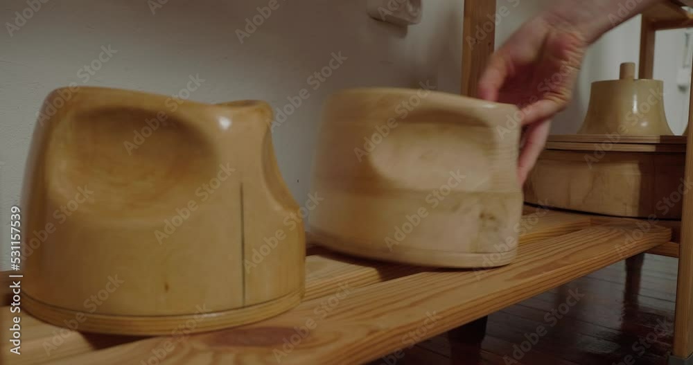 Woman arranges wooden molds for making hats in rows on shelf