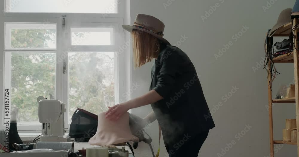Blonde woman steams felt hat body with iron turning mold Blonde woman steams felt hat body with iron turning mold