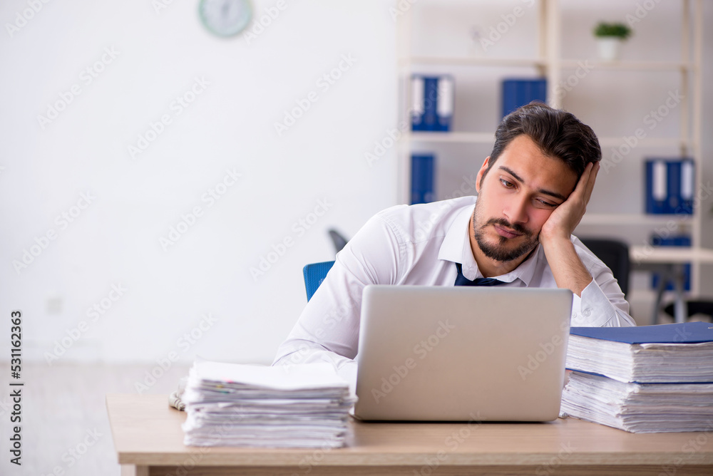 Young male employee unhappy with excessive work in the office Young male employee unhappy with excessive work in the office