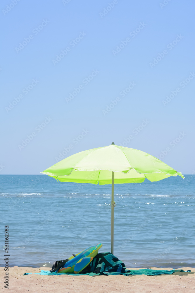 Light green beach umbrella in sand near sea on sunny day