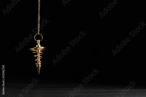 Stylish pendulum above table on black background, space for text. Hypnotherapy session