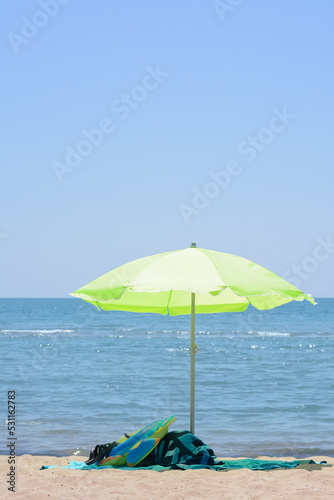 Fototapeta Naklejka Na Ścianę i Meble -  Light green beach umbrella in sand near sea on sunny day