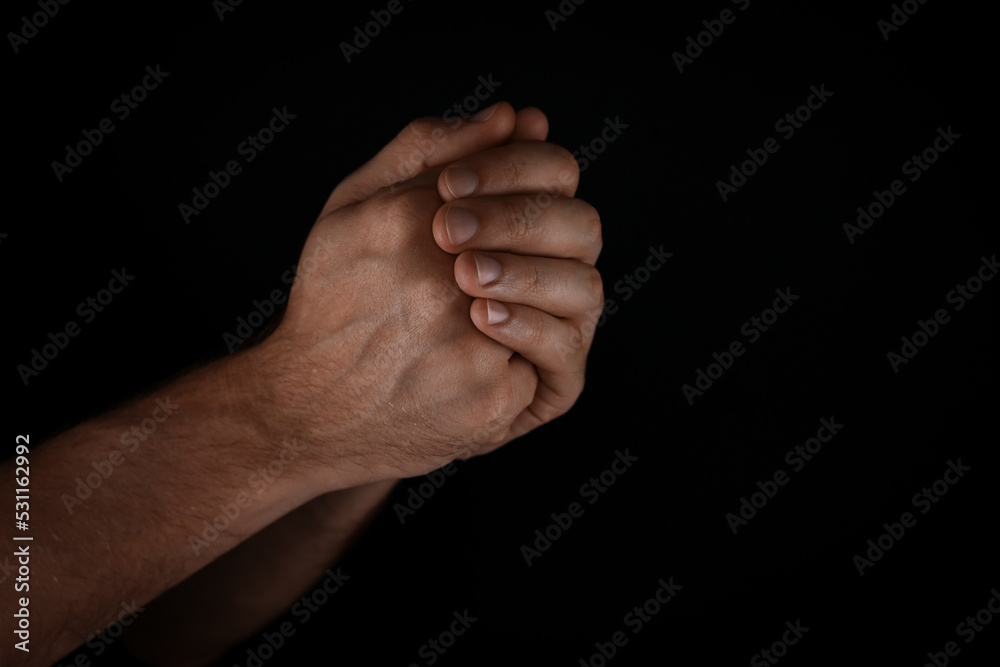 Man praying against black background, closeup view Man praying against black background, closeup view