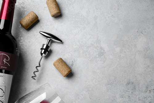 Fotografie Corkscrew with wine bottle, glass and stoppers on light grey stone table, flat lay