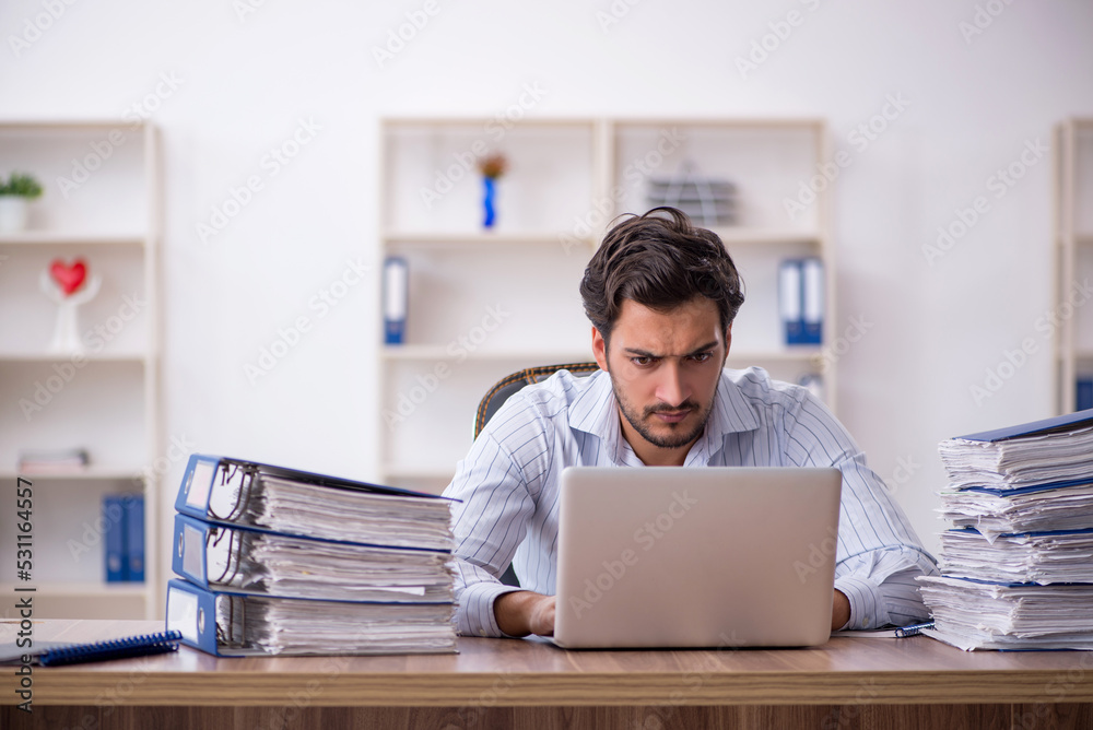 Young male employee unhappy with excessive work in the office Young male employee unhappy with excessive work in the office
