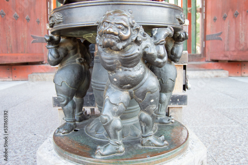 Fotografering buddhist demons holding the weight of an incense urn outside a buddhist temple