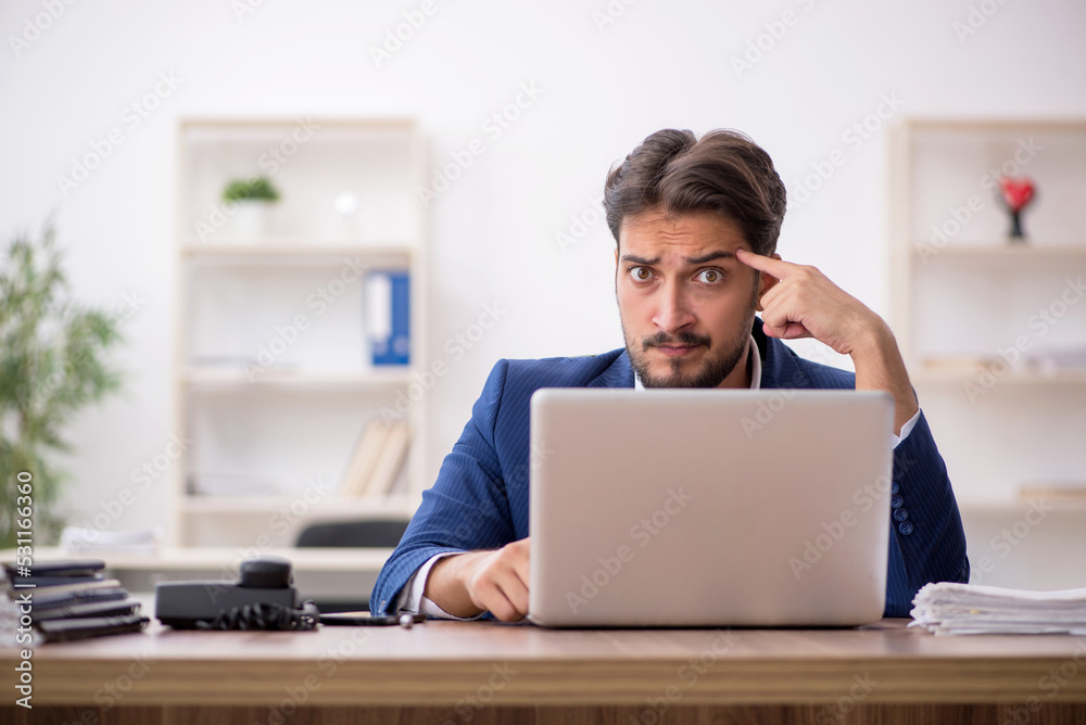 Young male employee unhappy with excessive work in the office Young male employee unhappy with excessive work in the office