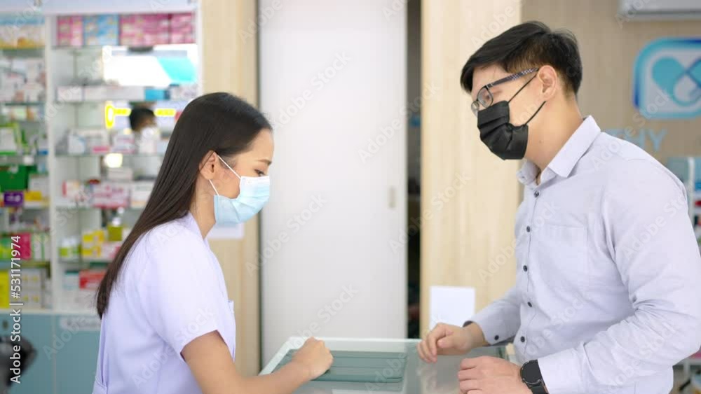 Asian woman pharmacist wear surgical face mask medication recommendation about medicine, drugs and supplements to male patient customer in drugstore. Medical pharmacy and healthcare providers concept. Asian woman pharmacist wear surgical face mask medication recommendation about medicine, drugs and supplements to male patient customer in drugstore. Medical pharmacy and healthcare providers concept.