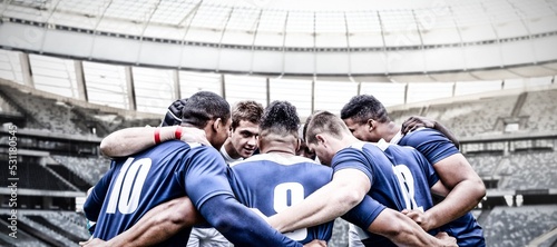 Digital composite image of team of rugby players standing in a huddle in sports stadium