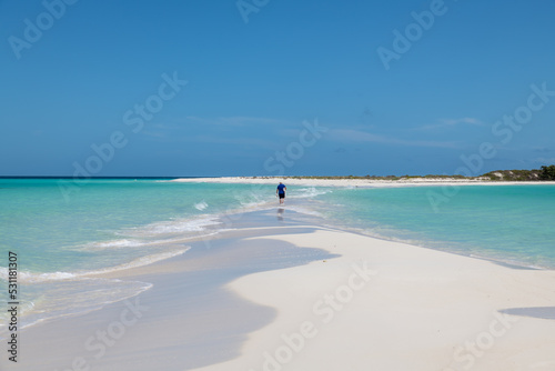 Cayo de Agua (Los Roques Archipelago), Venezuela: a lonely man walking on a sandbank between two small islands in the caribbean sea.