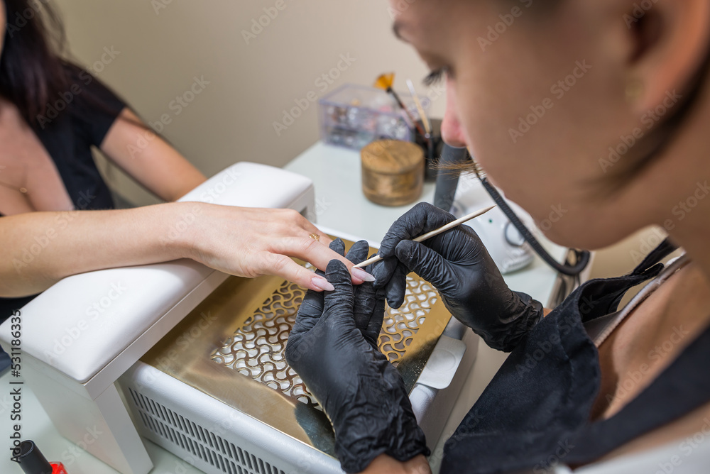 The master removes cuticles with a bamboo stick. Manicurist and client in a nail salon.