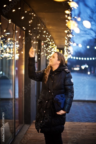 Portrait of a woman in the night city standing outside next to the Christmas lights 