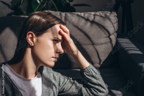 Close up of worried young woman sit on couch at home look in distance thinking pondering, anxious unhappy brunette female 20s suffer from mental psychological personal problems mourn or yearn concept