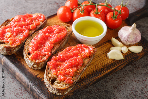 Catalan Pan con Tomate Spanish toasted bread rubbed with fresh garlic and ripe tomato, then drizzled with olive oil closeup on the wooden board on the table. Horizontal photo
