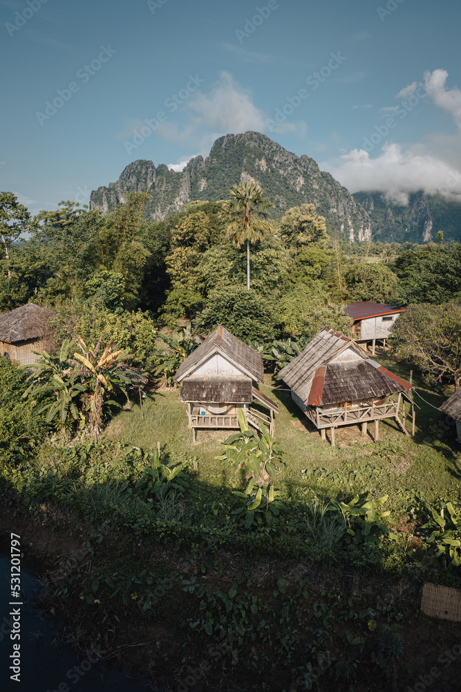 bungalows on the banks of the Nam Xong river on a sunny day with karst mountains in the background in rainy season