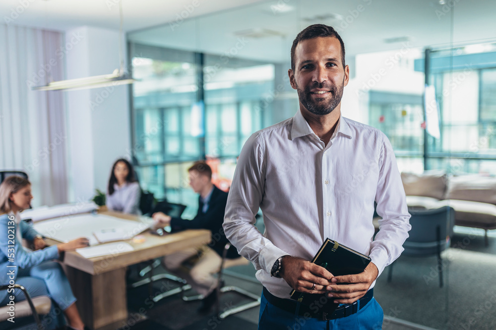 Fototapeta premium Portrait of a handsome young businessman in modern office smiling looking at the camera