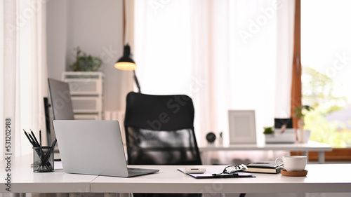 Horizontal image of laptop computer, documents and various office supplies on white table in modern interior © Prathankarnpap