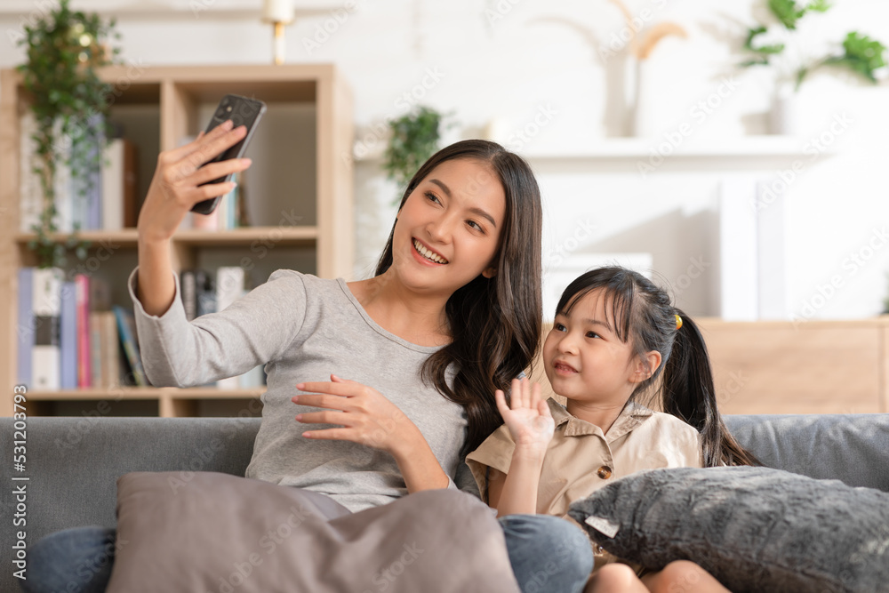 Asian young mother and her daughter have video call conference with family having fun together.Happiness Mom and little girl looking at mobile phone and waving hand with video chat to grandmother Asian young mother and her daughter have video call conference with family having fun together.Happiness Mom and little girl looking at mobile phone and waving hand with video chat to grandmother