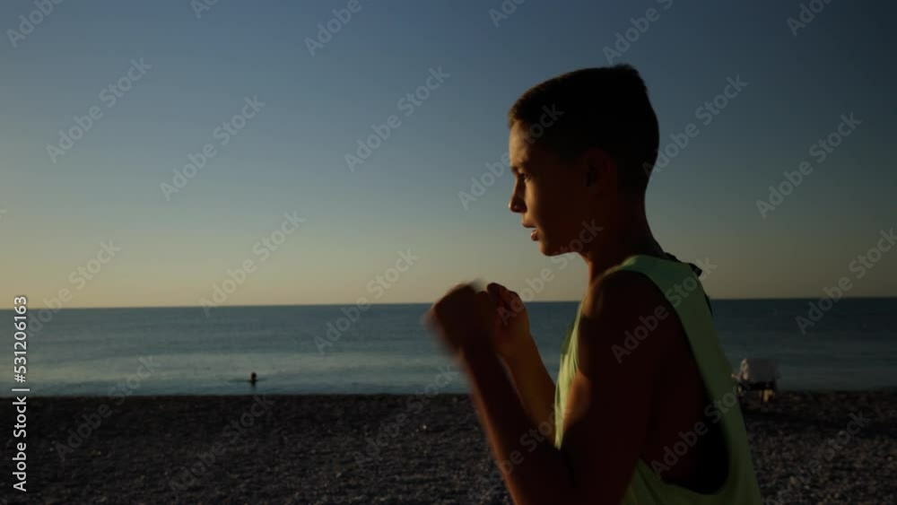 Young male boxer or karate fighter training on the beach during sunrise. Silhouette shot of boy doing shadow boxing in the morning. High quality 4k footage Young male boxer or karate fighter training on the beach during sunrise. Silhouette shot of boy doing shadow boxing in the morning. High quality 4k footage