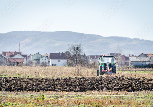 Winter agricultural landscape. Winter plowing arable land with green tractor.