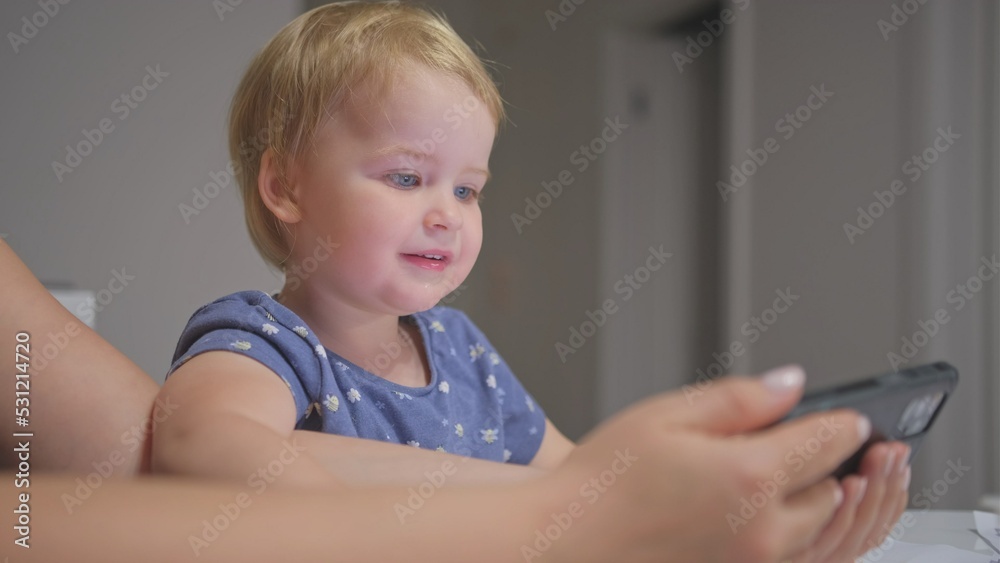Happy Caucasian Toddler Baby Girl Watching Video and Playing on Smartphone with Mother Making Funny Faces and Showing Emotions Happy Caucasian Toddler Baby Girl Watching Video and Playing on Smartphone with Mother Making Funny Faces and Showing Emotions
