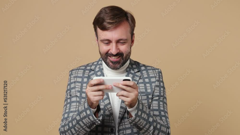 Young gambling employee business man corporate lawyer in classic grey suit jacket use play racing on mobile cell phone gadget smartphone work in office isolated on plain pastel light beige background Young gambling employee business man corporate lawyer in classic grey suit jacket use play racing on mobile cell phone gadget smartphone work in office isolated on plain pastel light beige background