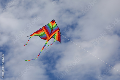 kite with the many colors of the rainbow flying high attached to a string