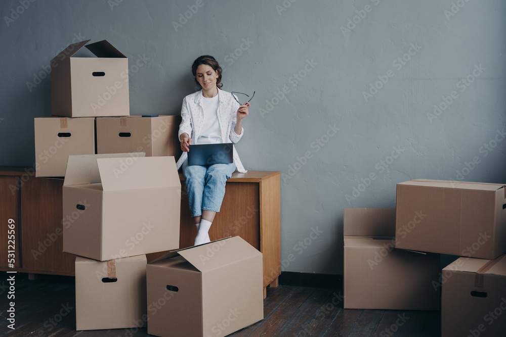 Female with carton boxes searching moving company at laptop for relocation. Transportation service Female with carton boxes searching moving company at laptop for relocation. Transportation service