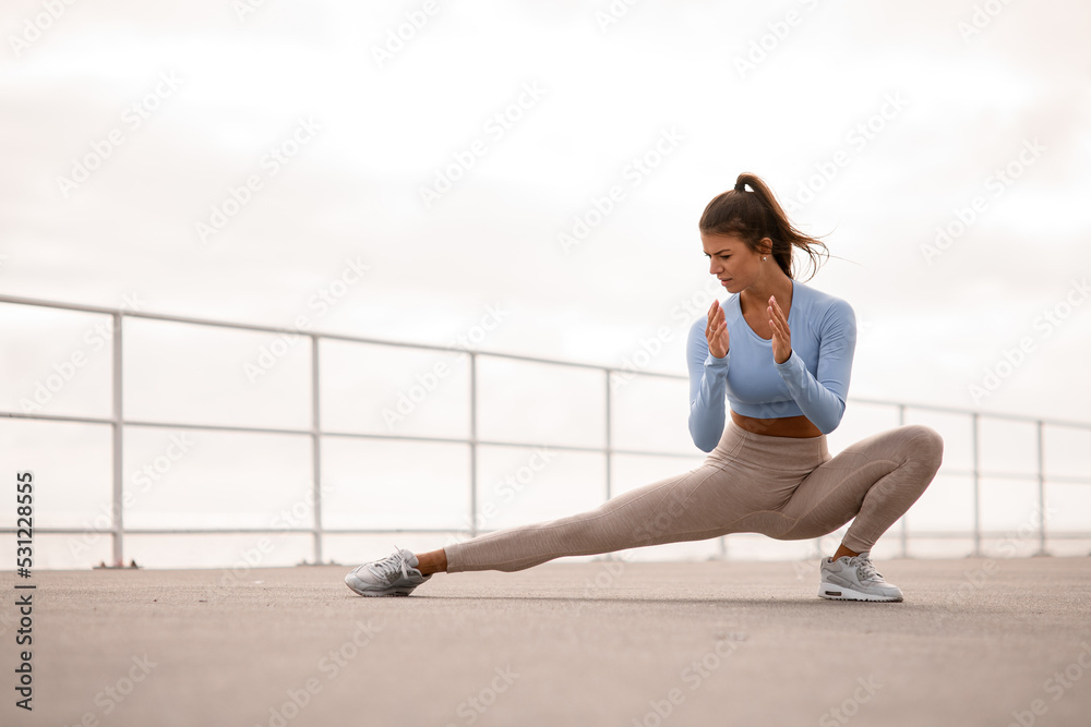 Fototapeta premium sporty woman stretching her body and doing side lunge exercises outdoor
