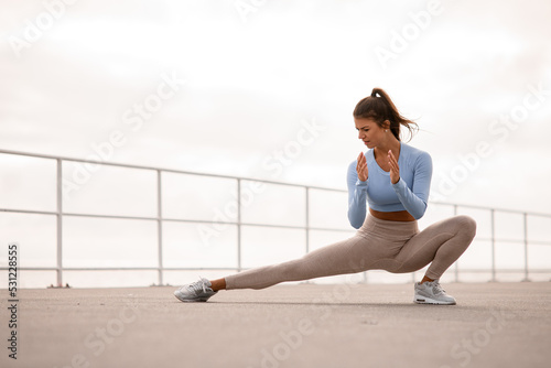 Fototapeta Naklejka Na Ścianę i Meble -  sporty woman stretching her body and doing side lunge exercises outdoor