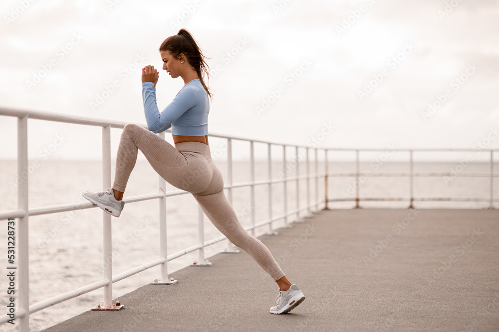 view on woman warming up her muscles and leans with one foot on the fence