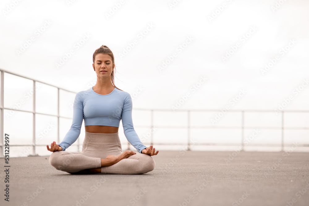 Attractive woman with closed eyes sitting in lotus position outdoor.
